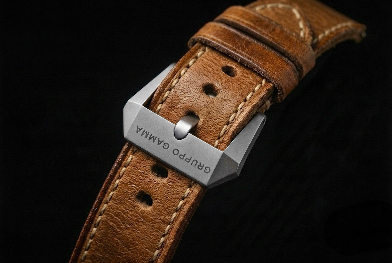 A close-up of a brown leather watch strap with a stainless steel buckle engraved with the brand name 'GRUPO GAMMA', set against a solid black background.