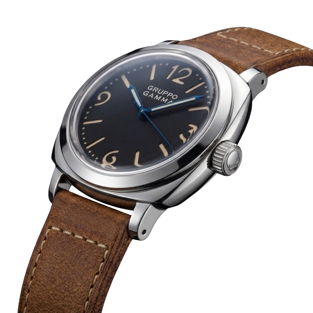 A close-up shot of a Gruppo Gamma wristwatch featuring a stainless steel case, black dial and blue hands, and a brown leather strap.