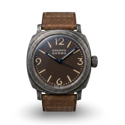 A Gruppo Gamma wristwatch with an aged steel dark gray case, a tropical dark brown dial with beige Arabic numerals and steel blue hands, and a brown leather strap.