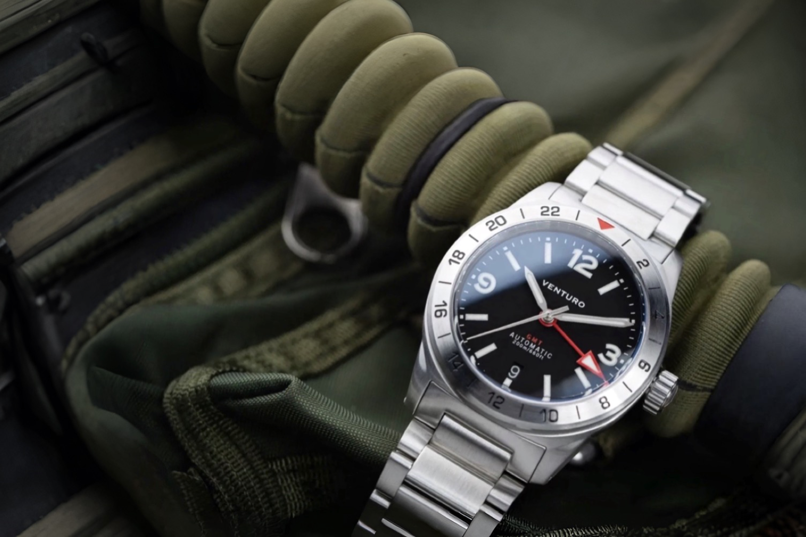 Silver watch with black dial on a green military-style glove
